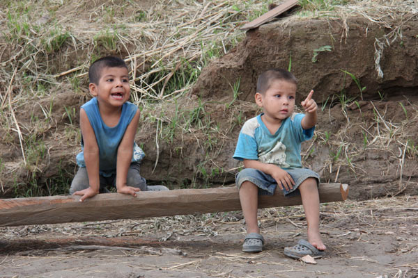 Boys watch boats passersby on the riverbank in Rurrenabaque, Bolivia. Photo by Barbara Fraser